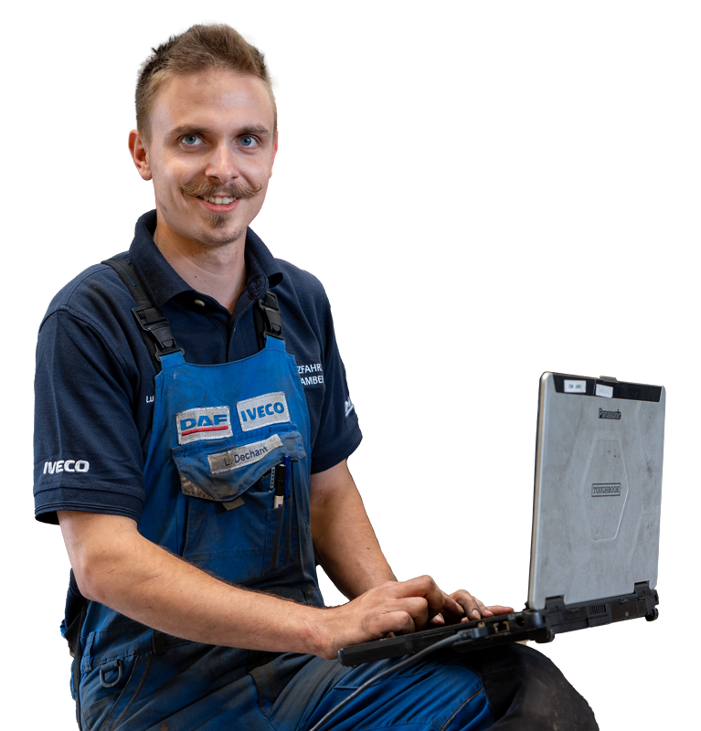 Mitarbeiter in blauer Arbeitskleidung sitzt mit Laptop in einer Werkstatt.