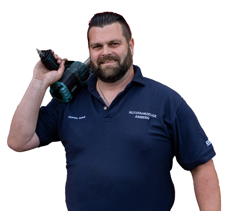 Mann mit Bart hält eine Bohrmaschine in der Hand, trägt ein blaues Hemd mit dem Namen Thomas.