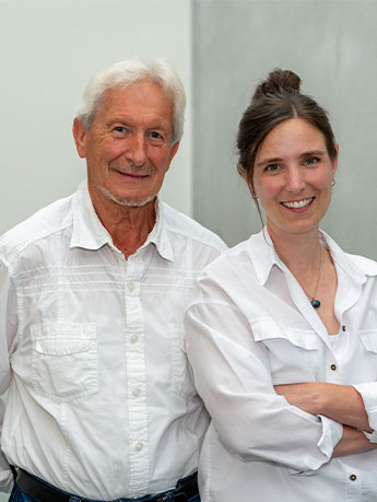 Zwei Personen, ein älterer Mann und eine jüngere Frau, stehen nebeneinander und lächeln in die Kamera.