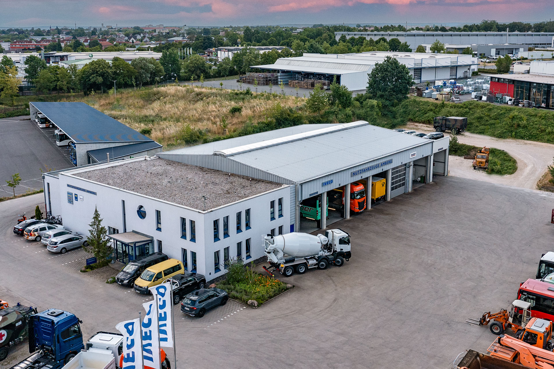Luftaufnahme eines Lagerhauses mit mehreren Fahrzeugen, darunter ein Betonmischer und Nutzfahrzeuge.